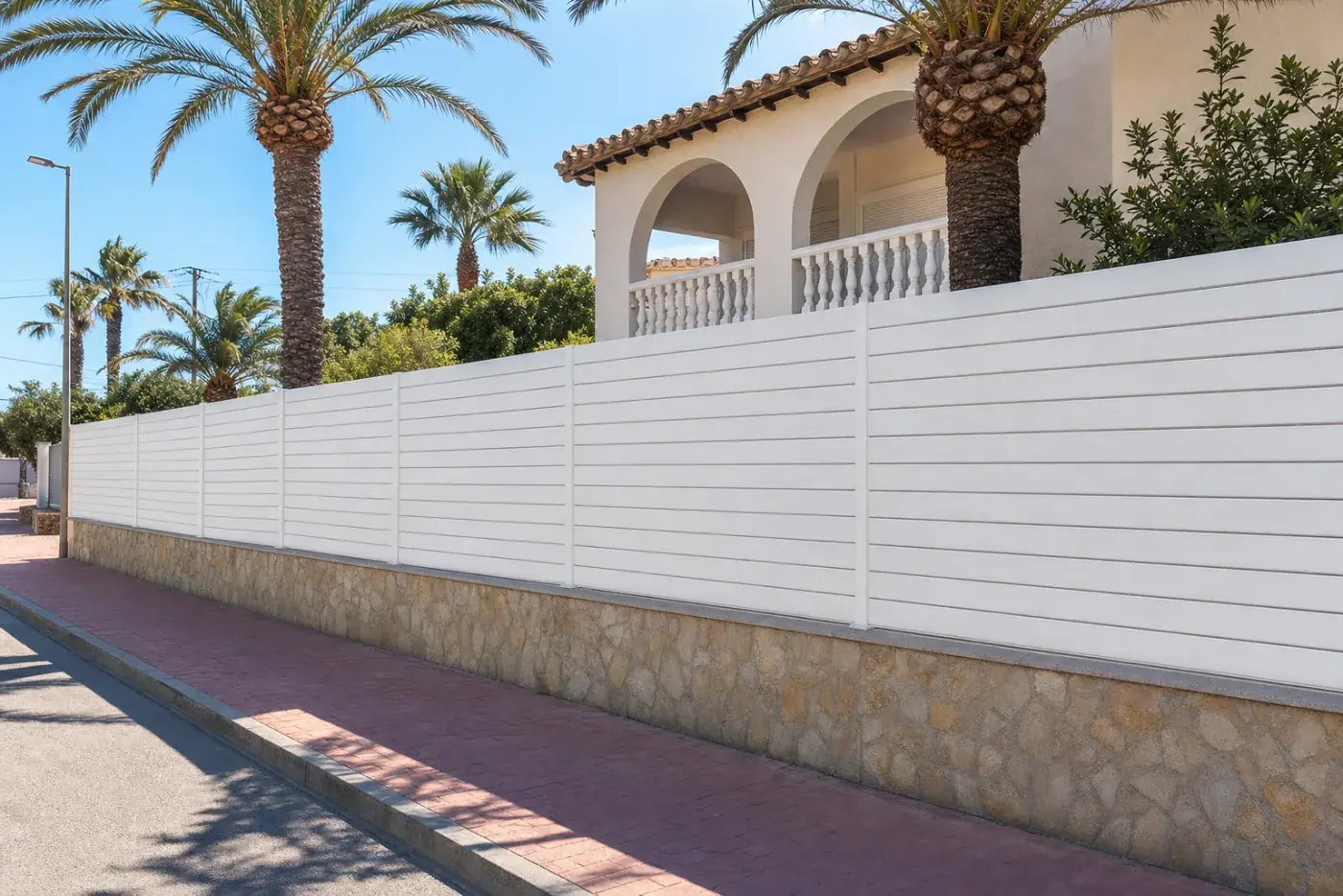 Tanca semi-oberta blanca davant d'una casa mediterrània amb palmeres